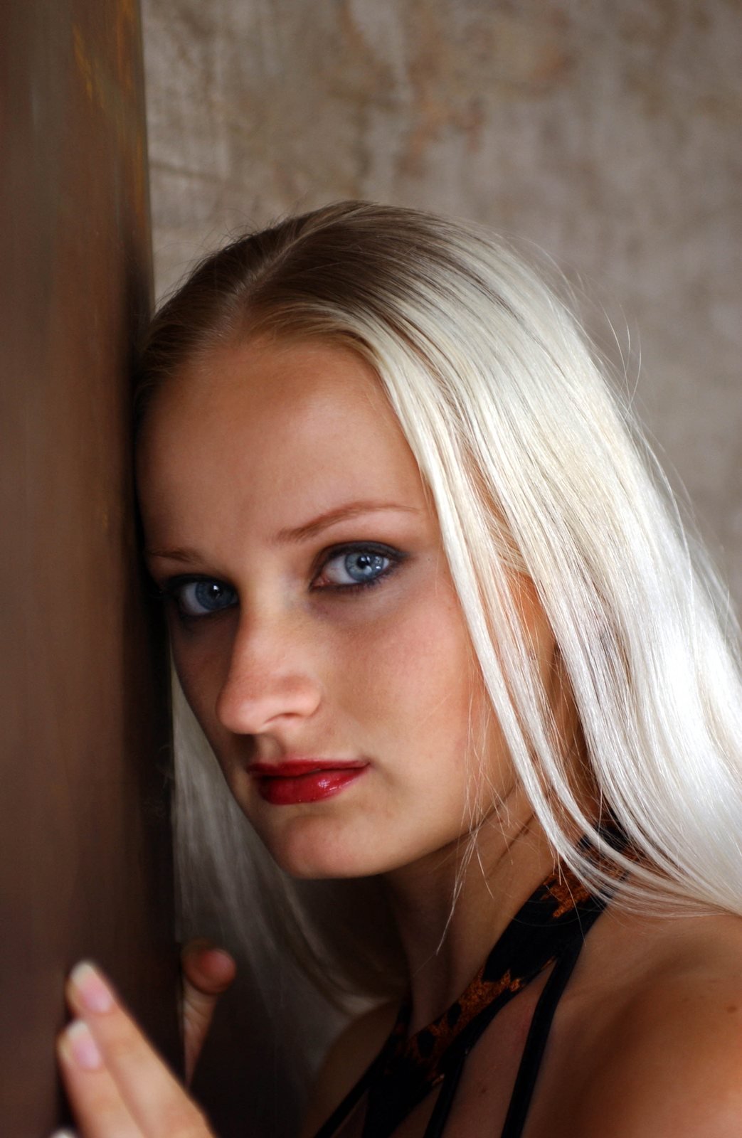 A woman with long platinum hair and red lipstick leans against a wooden post, looking at the camera