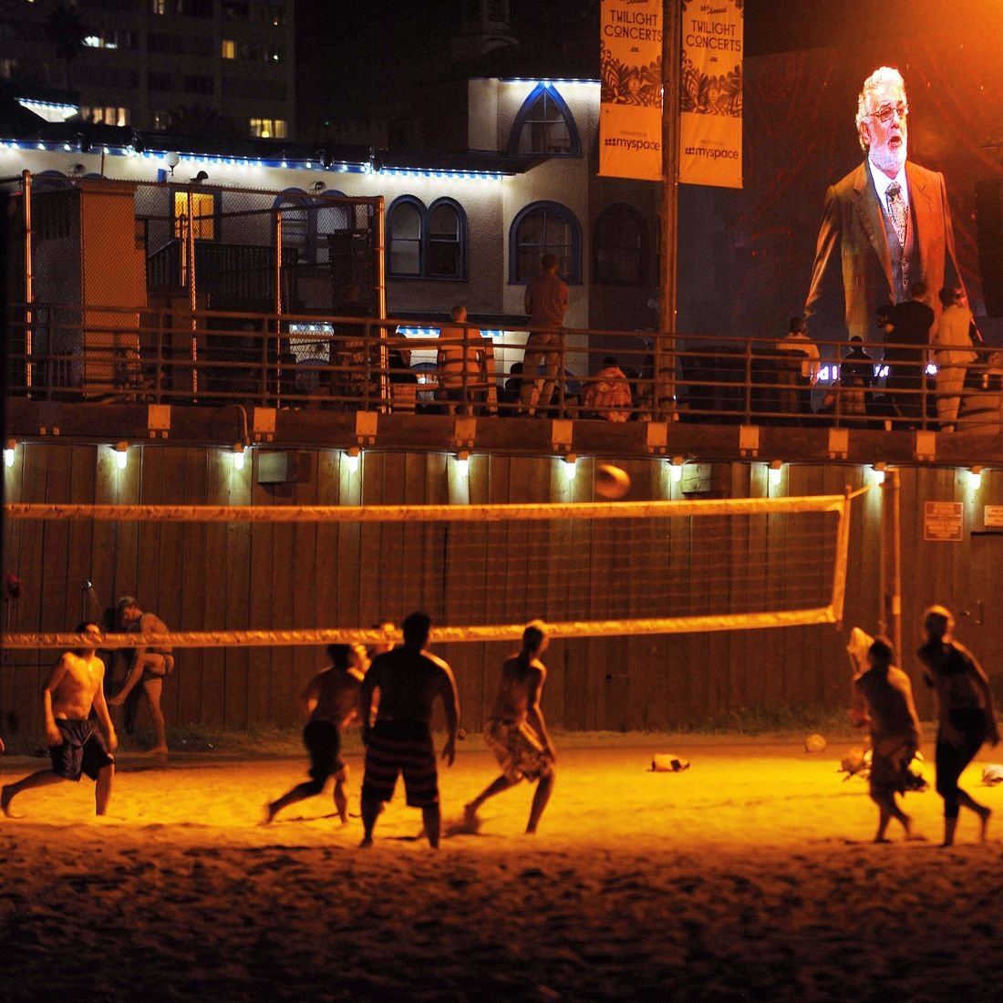 Players on a beach volleyball court at night under lights