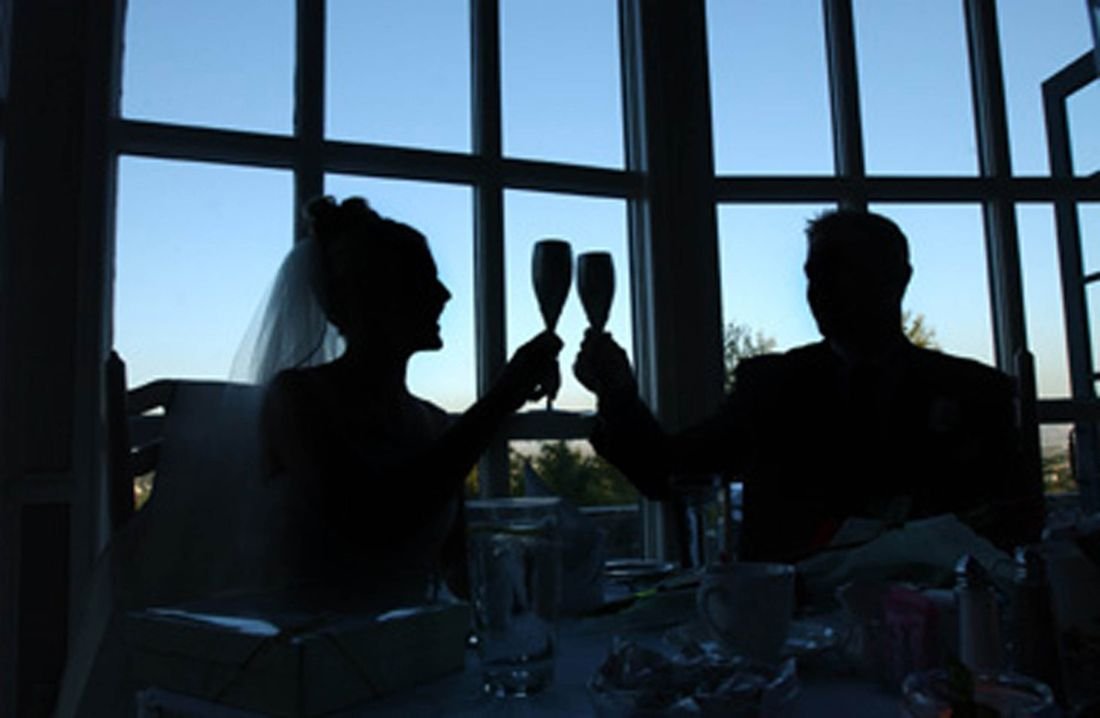 Silhouettes of two people raising glasses against tall windows