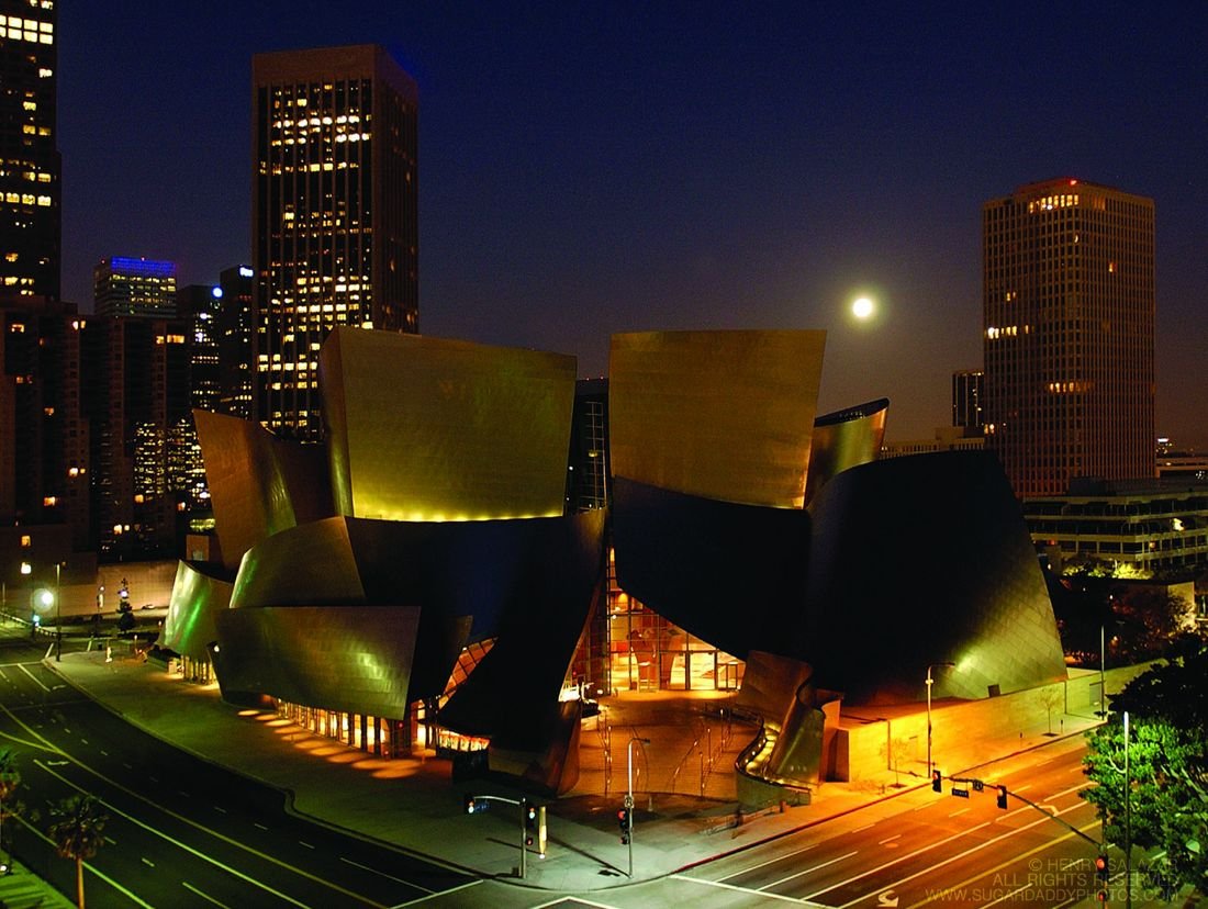 Walt Disney Concert Hall lit gold against the downtown Los Angeles skyline at night