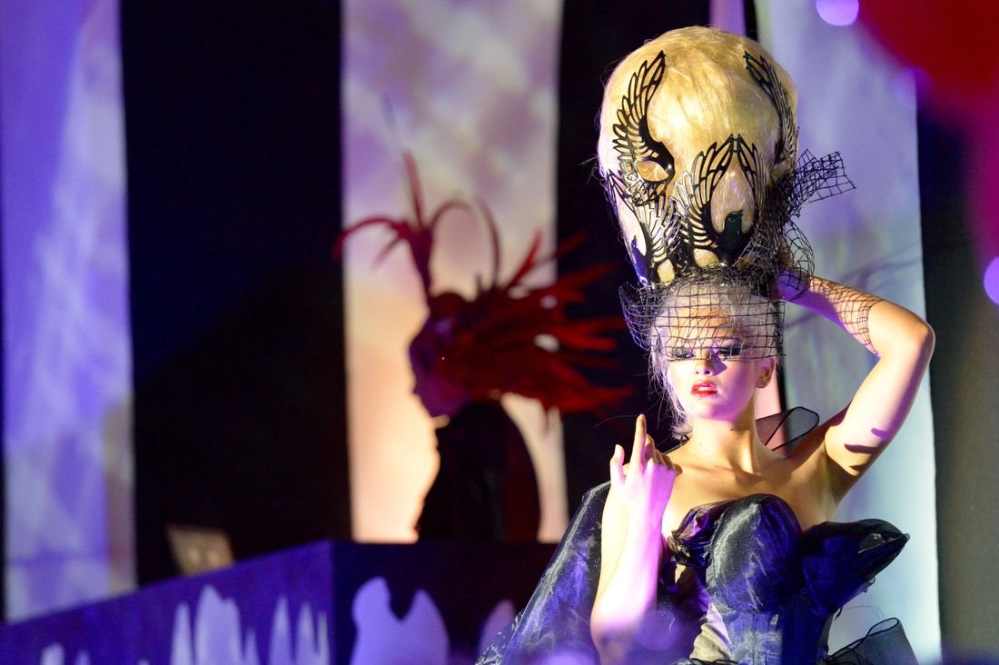 A performer in an ornate gold headdress and costume under stage lights